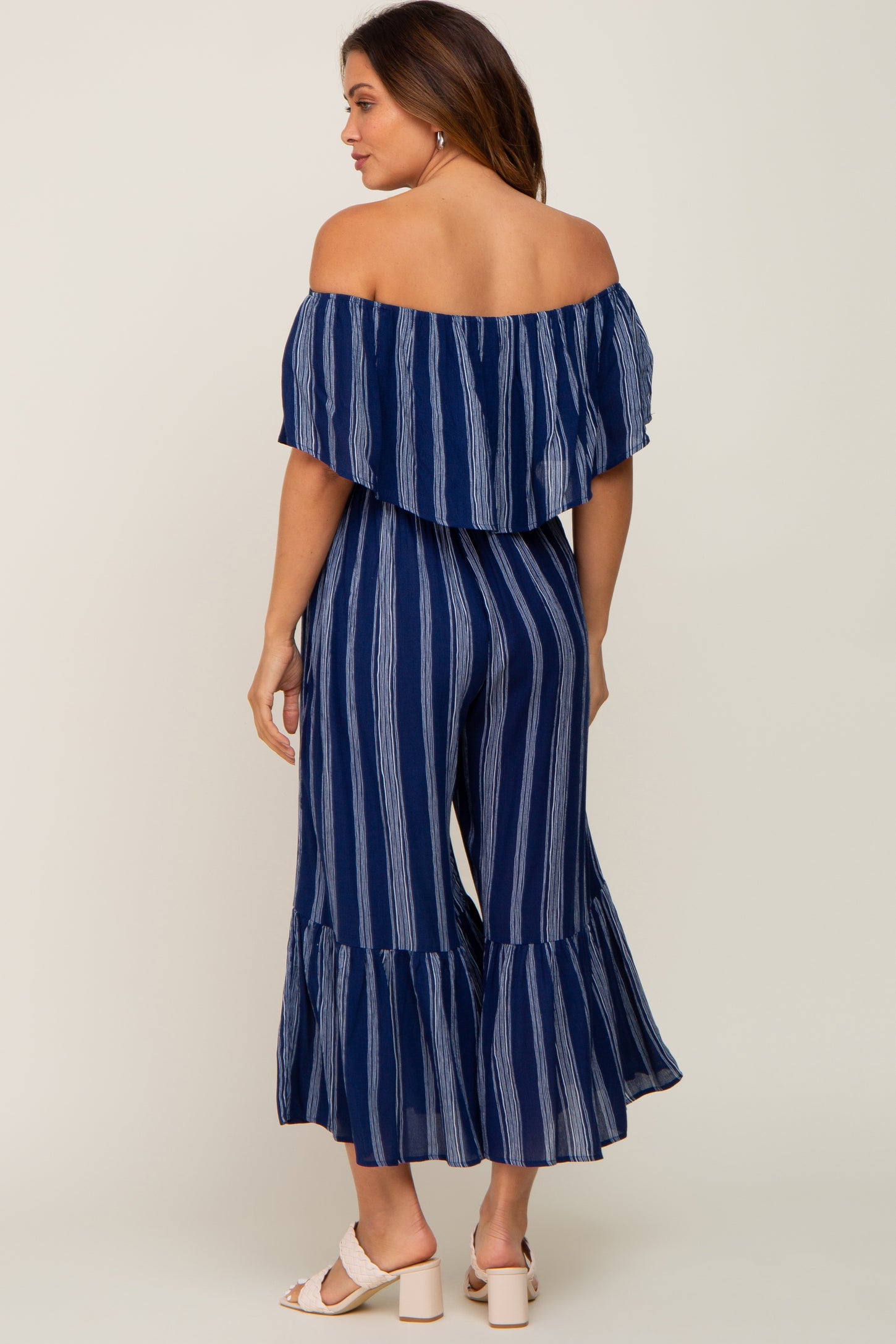woman wearing a navy blue and white striped off-the-shoulder maternity jumpsuit with ruffled hem