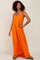 Woman with curly hair wearing a long orange sleeveless maxi dress with tie straps and sandals