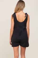 woman wearing a black sleeveless maternity romper with tie details on the shoulders, showing a relaxed fit and open back