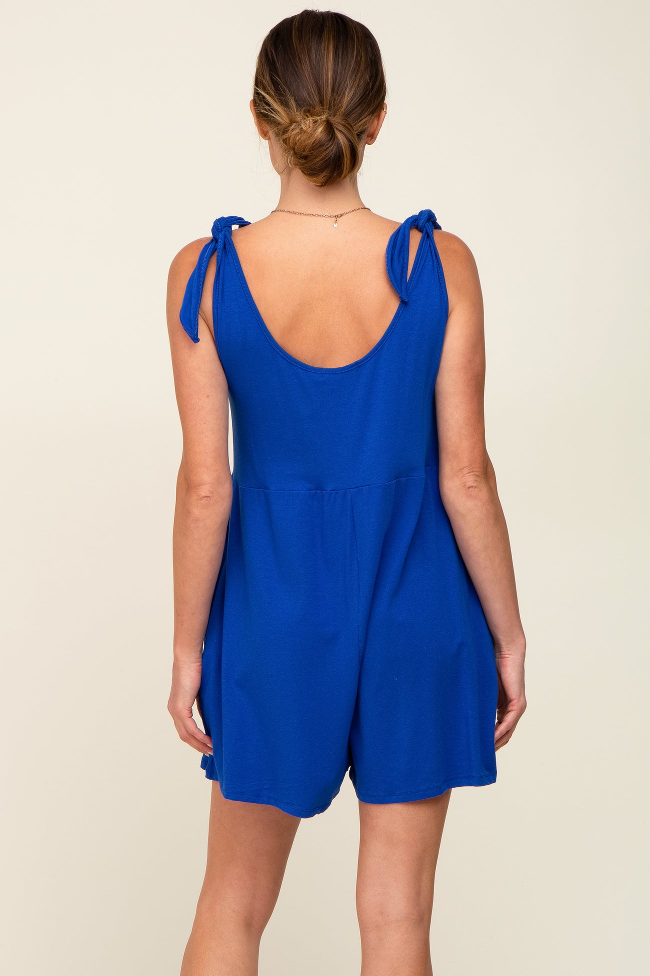 woman wearing a blue sleeveless romper with tie shoulder straps, showing the back view