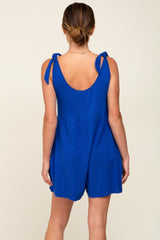 woman wearing a blue sleeveless romper with tie shoulder straps, showing the back view