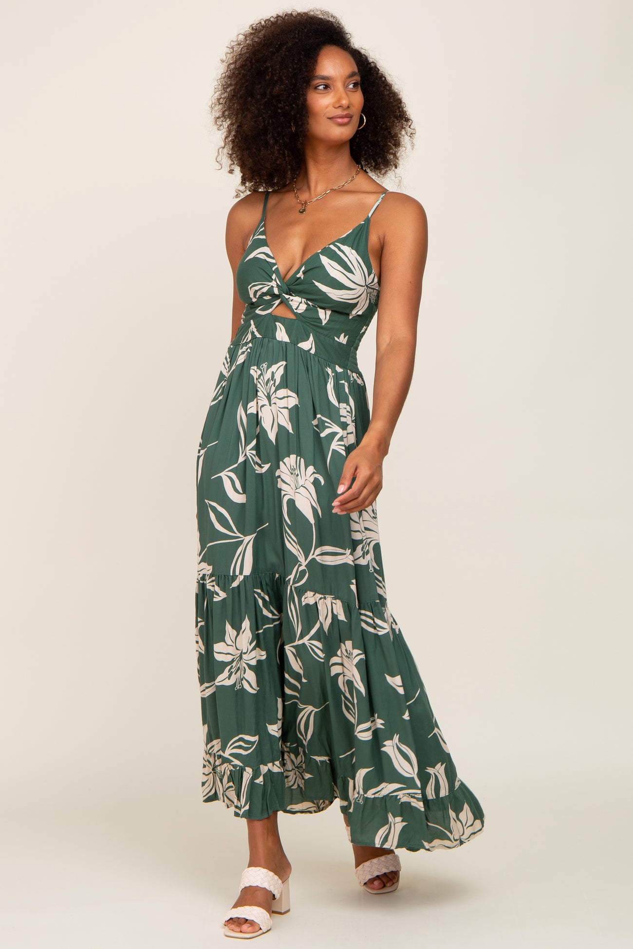 Woman wearing a green floral maxi dress with a cutout waist and tiered skirt against a neutral background