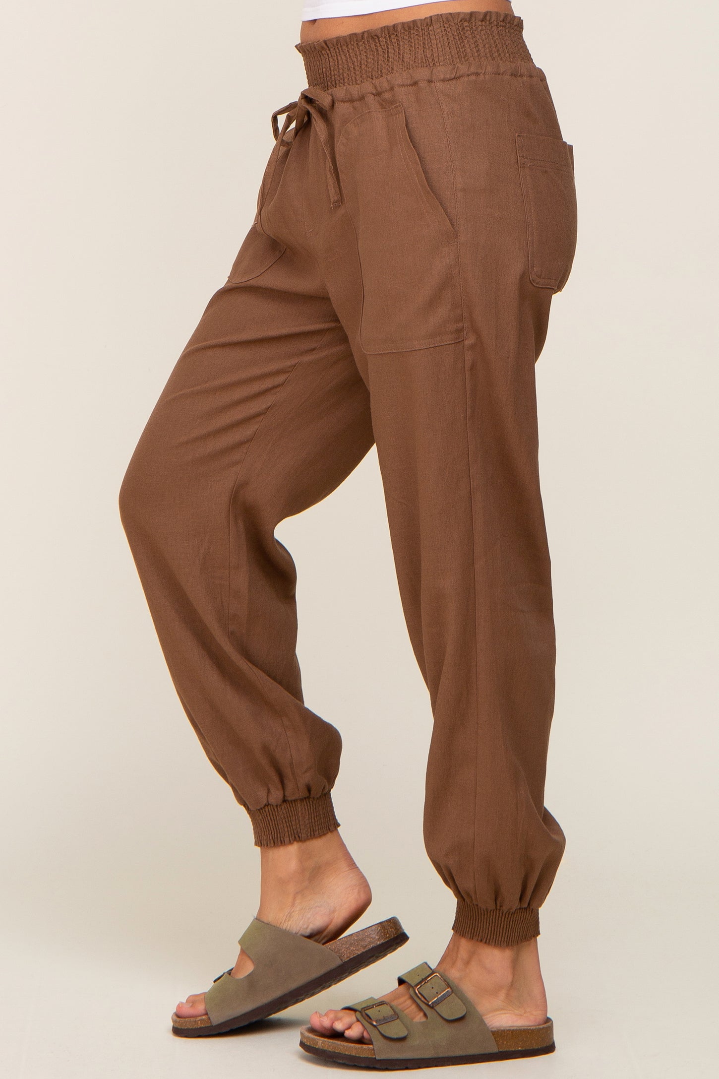 person wearing brown linen jogger pants with drawstring waist and elastic cuffs paired with olive green slide sandals