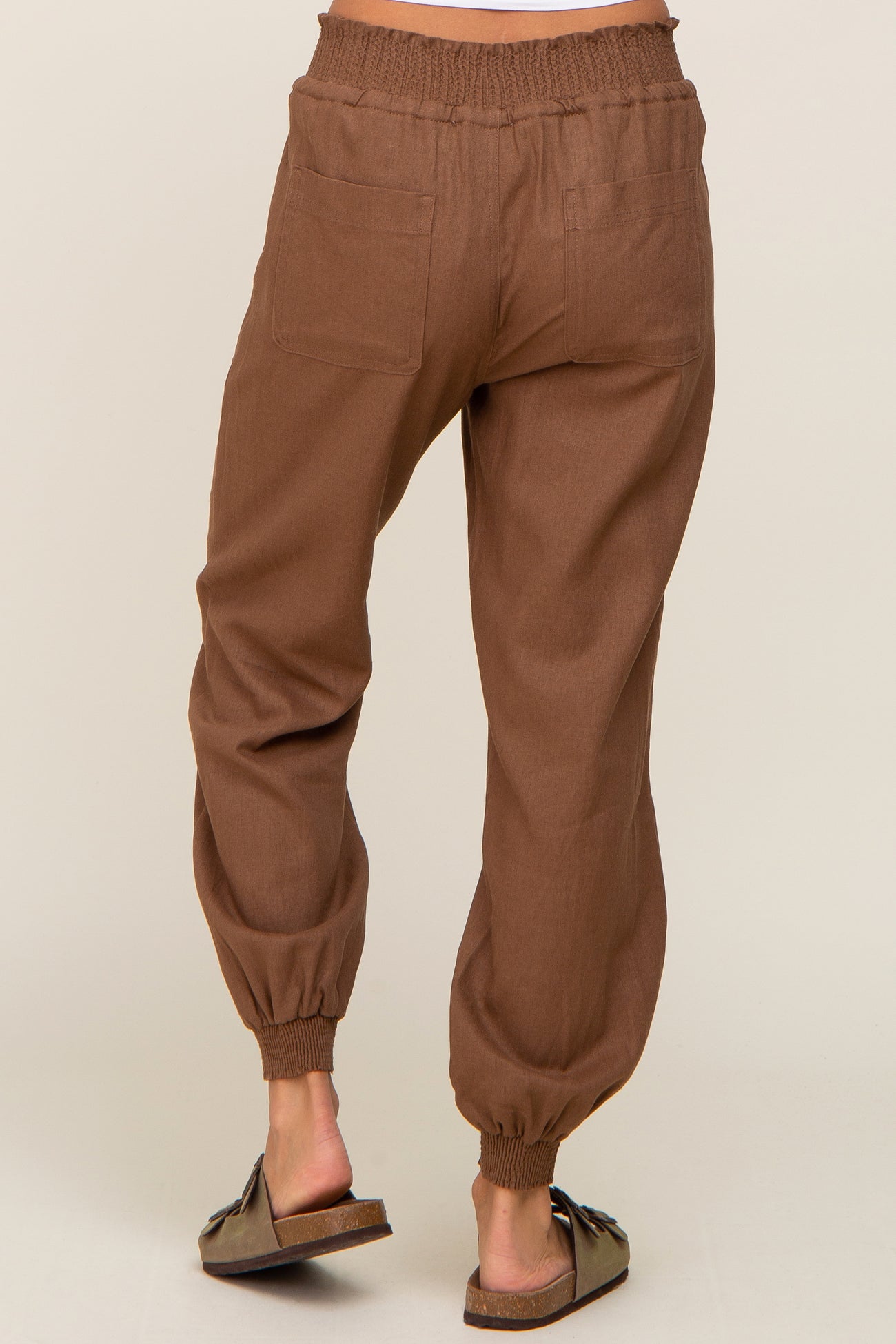 Back view of brown linen jogger pants with elastic waistband and cuffs worn with slide sandals