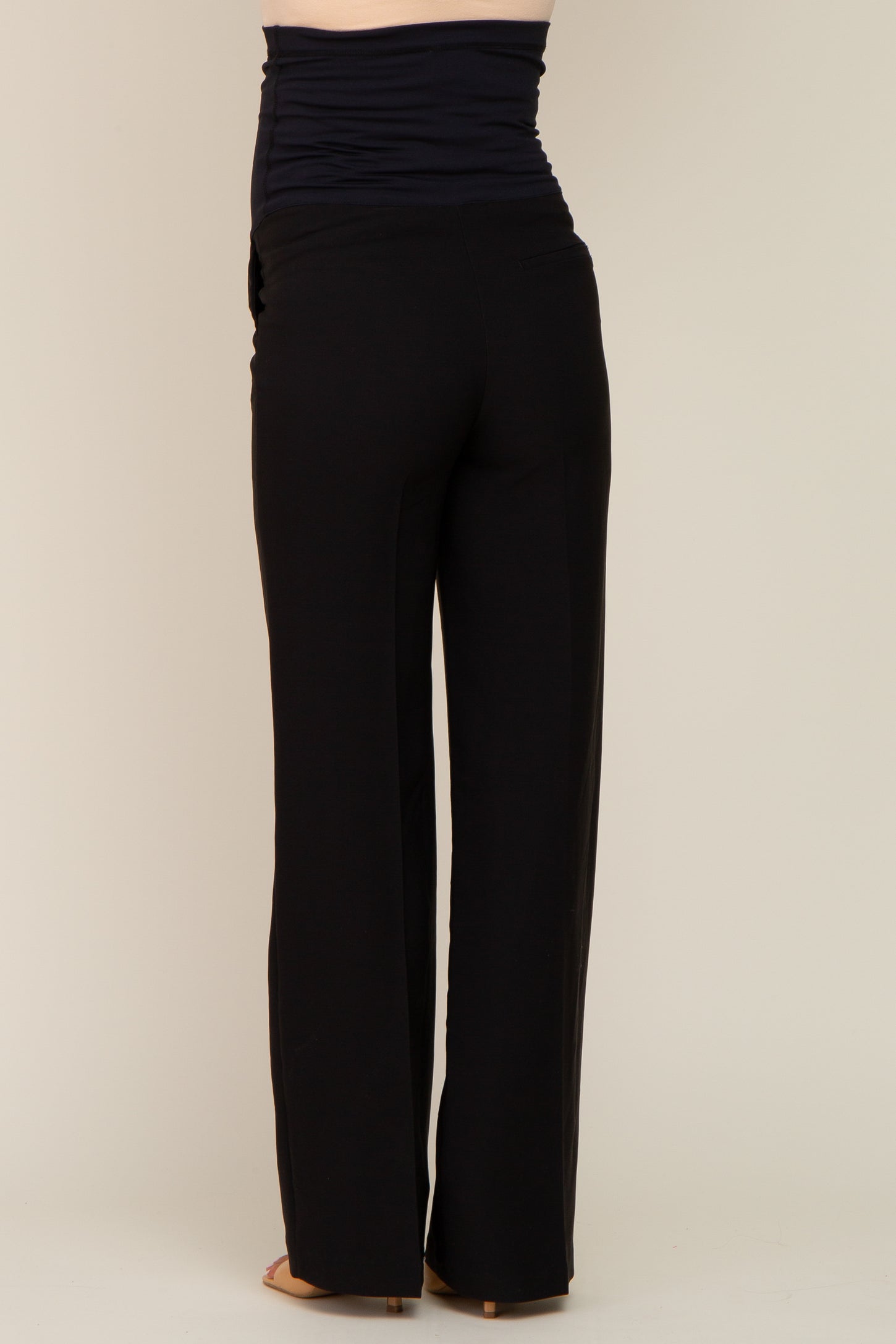 woman wearing black maternity pants with a ruched waistband, standing sideways to show the back view