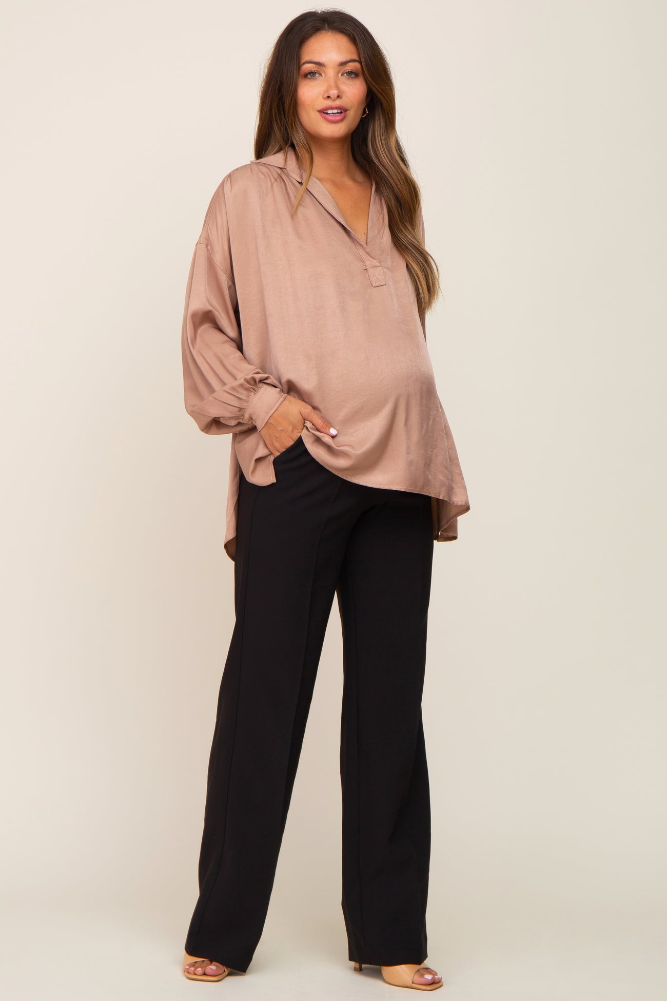 woman wearing a taupe maternity blouse with a v-neck and long sleeves, paired with black maternity pants and showing her baby bump