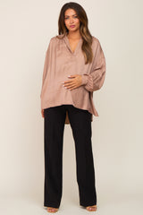 woman wearing a beige maternity blouse with a loose fit and long sleeves, cradling her baby bump with black pants