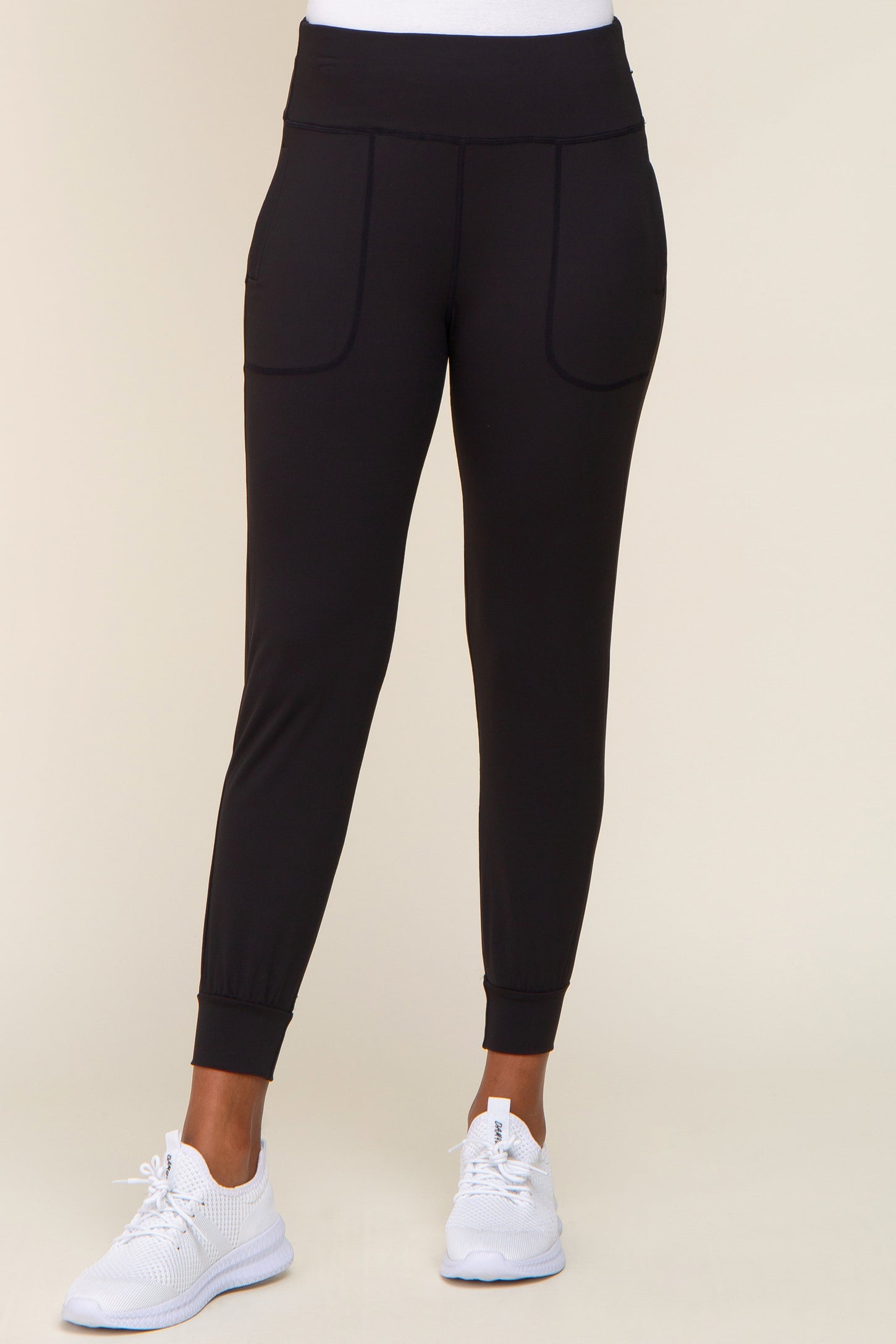 woman wearing black high-waisted joggers with front pockets and white athletic sneakers