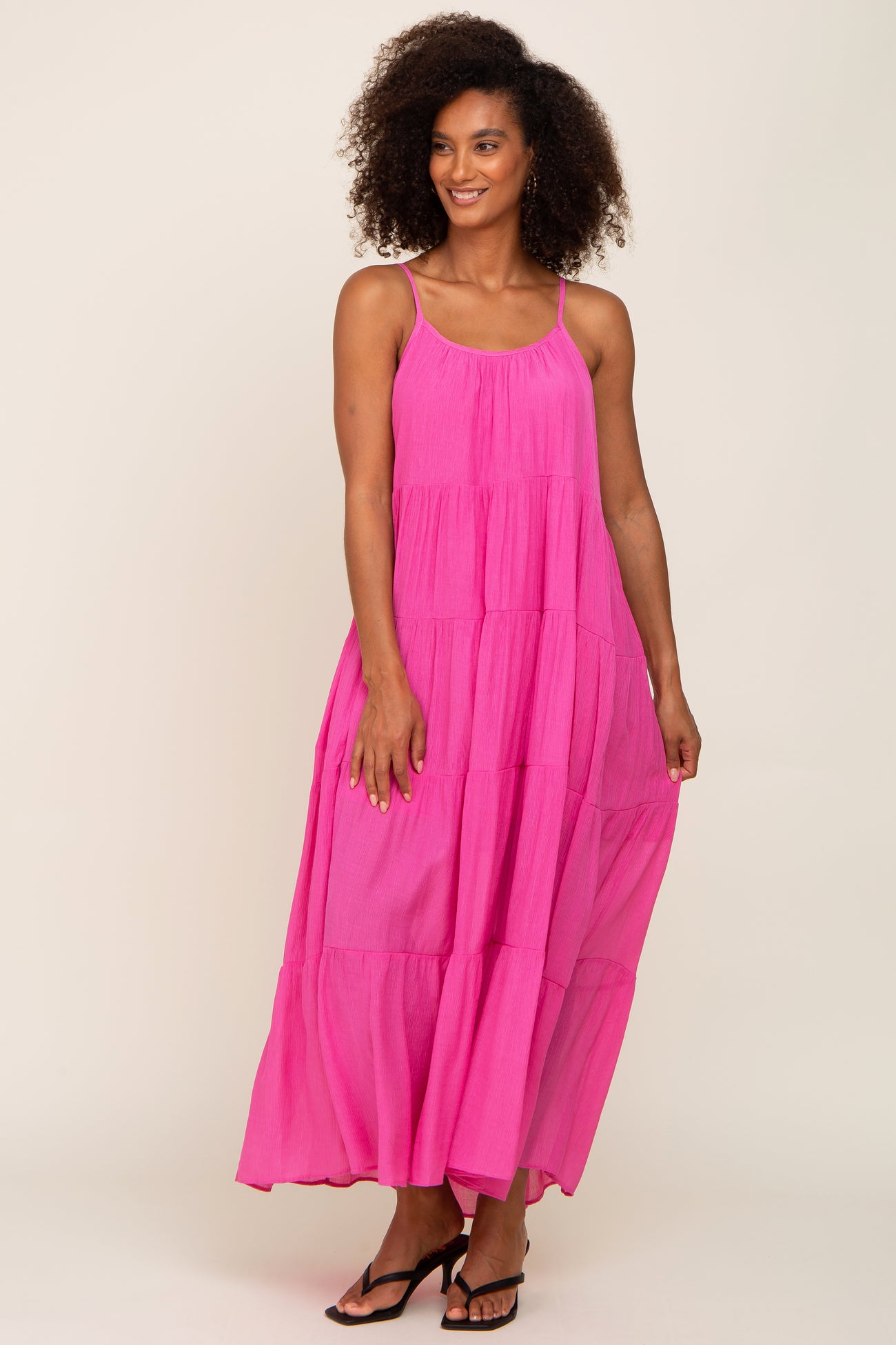 woman with curly hair wearing a hot pink tiered maxi dress with spaghetti straps and black sandals