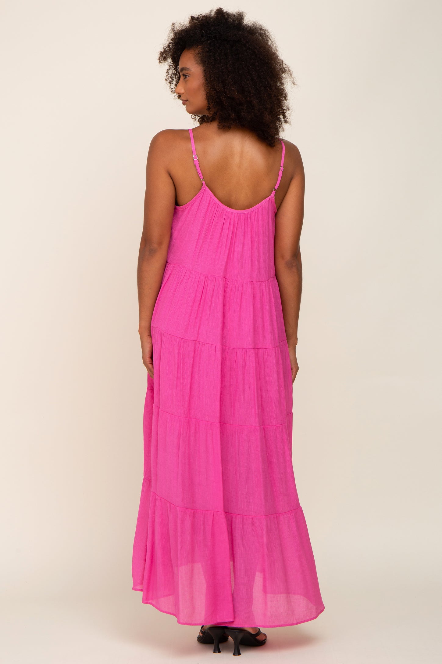 Woman from behind wearing a tiered hot pink maxi dress with spaghetti straps and black heels