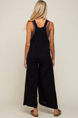 back view of a woman wearing black wide leg overalls and a brown tank top
