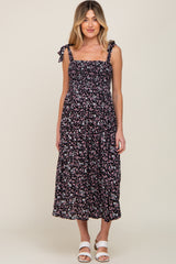 woman wearing a black floral print maternity dress with adjustable tie straps and a flowy silhouette
