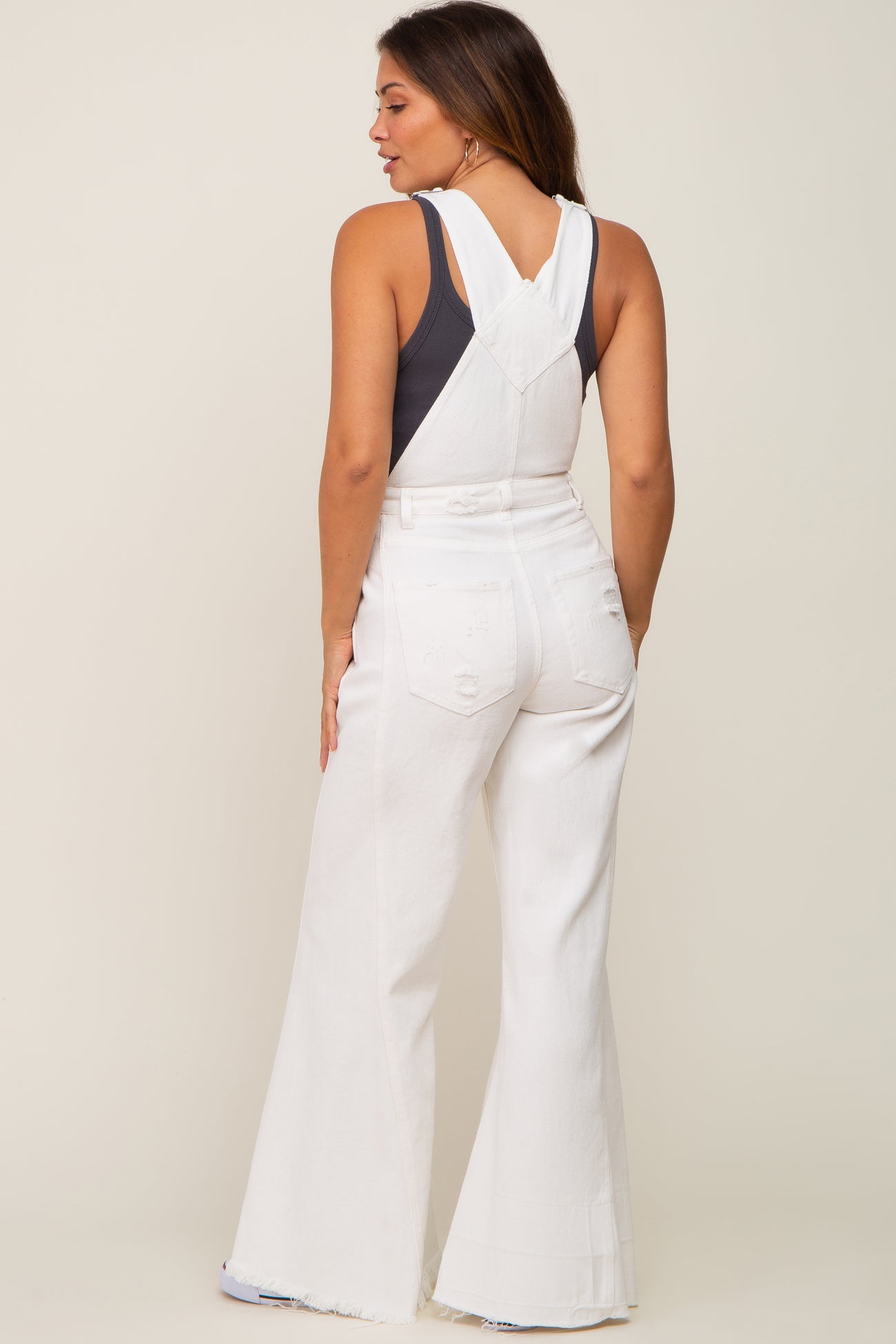 Woman wearing white denim flare overalls and a black tank top viewed from the back