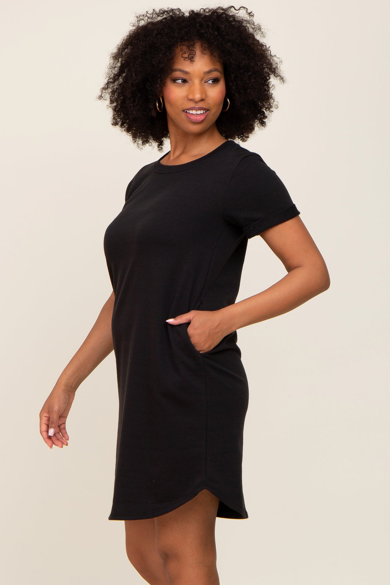 woman wearing a black short sleeve dress with a relaxed fit and side pockets, standing sideways with a smile