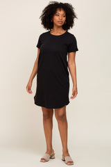 woman wearing a black short sleeve dress styled as a relaxed fit, standing on a plain background