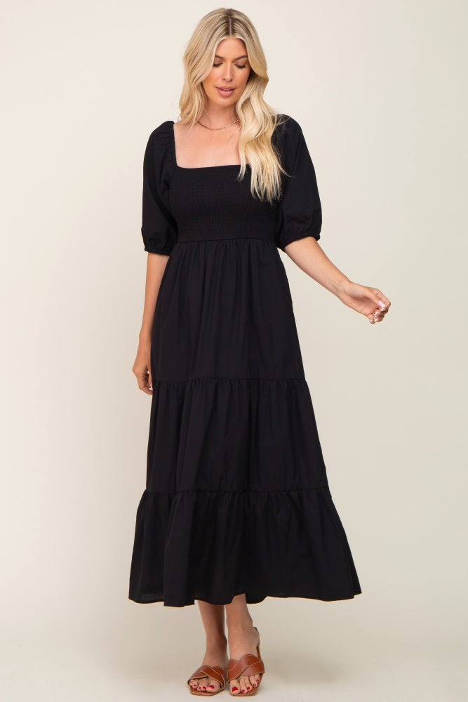woman wearing a black puff sleeve maxi dress with a square neckline and tiered skirt