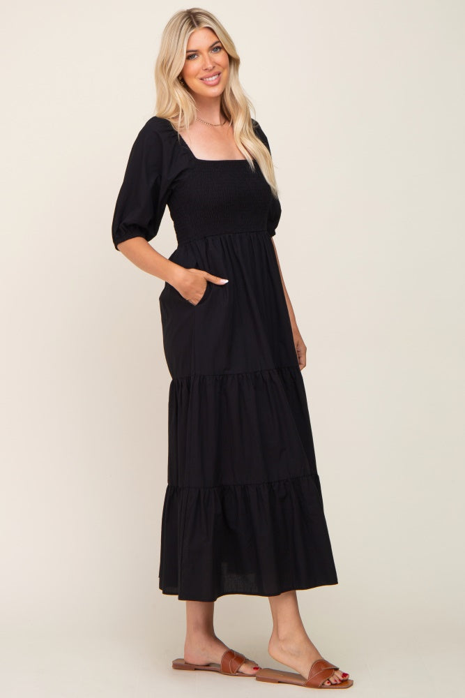 woman wearing a black puff sleeve maxi dress with a smocked bodice and pockets, standing sideways