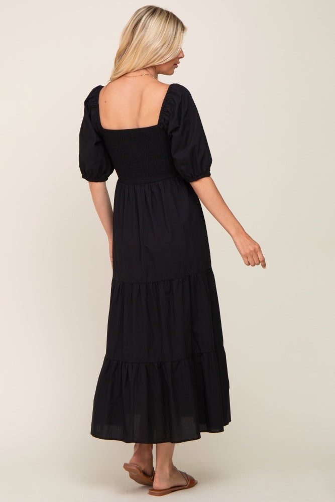 woman wearing a black tiered maxi dress with puff sleeves and a smocked bodice, shown from the back