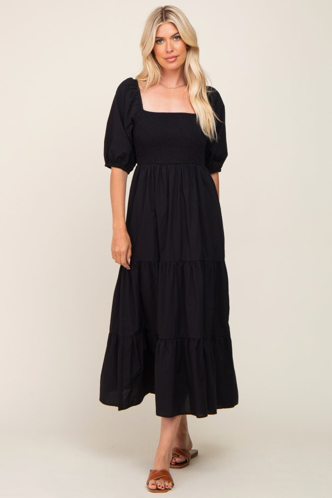 Woman wearing a black smocked midi dress with puff sleeves and a tiered skirt