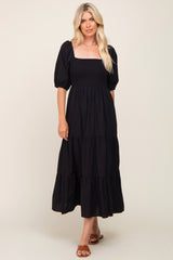 Woman wearing a black smocked midi dress with puff sleeves and a tiered skirt