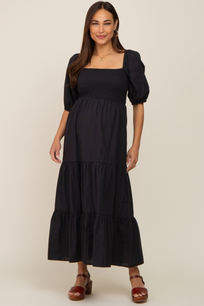 woman wearing a black maternity maxi dress with puff sleeves and a smocked bodice, showing off her baby bump