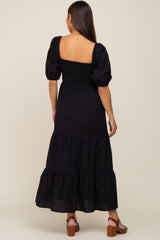 woman wearing a black tiered maternity dress with puff sleeves and a smocked back