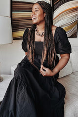 woman wearing a black puff sleeve maxi dress with a smocked bodice, sitting and smiling