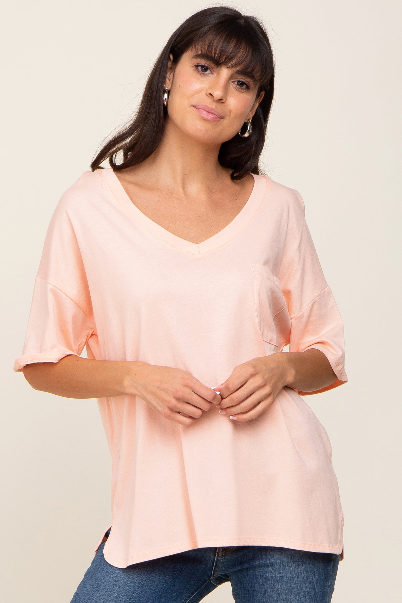 woman wearing a light peach v-neck t-shirt with a front pocket and blue jeans