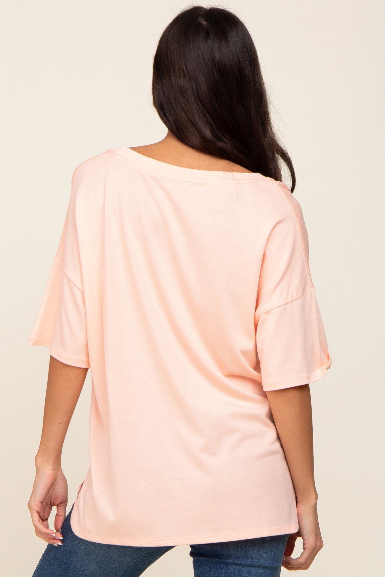 back view of a woman wearing a light peach short sleeve oversized t-shirt and blue jeans