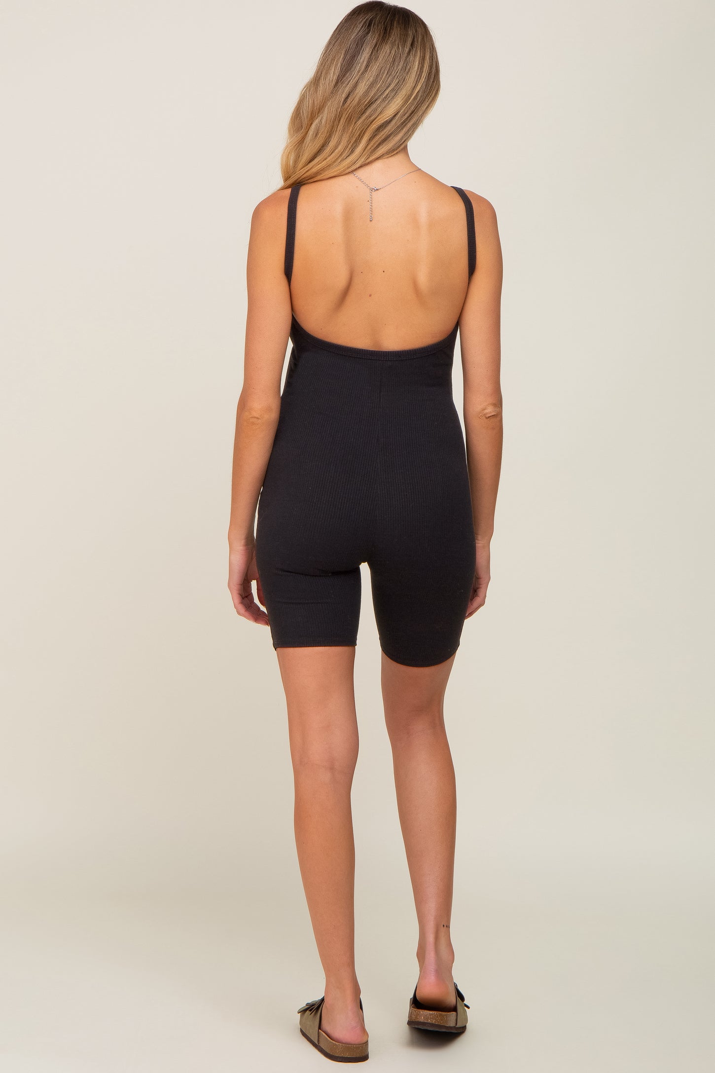 Back view of a woman wearing a black ribbed scoop back maternity romper with biker shorts