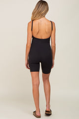 Back view of a woman wearing a black ribbed scoop back maternity romper with biker shorts