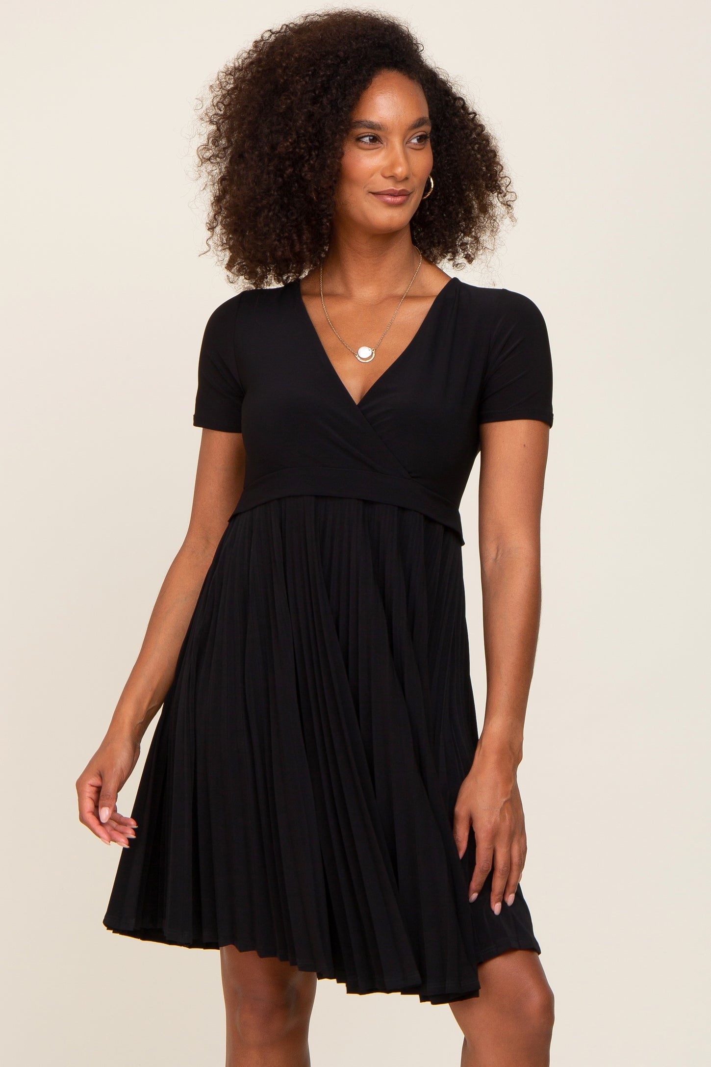 woman with curly hair wearing a black short sleeve v-neck pleated maternity dress