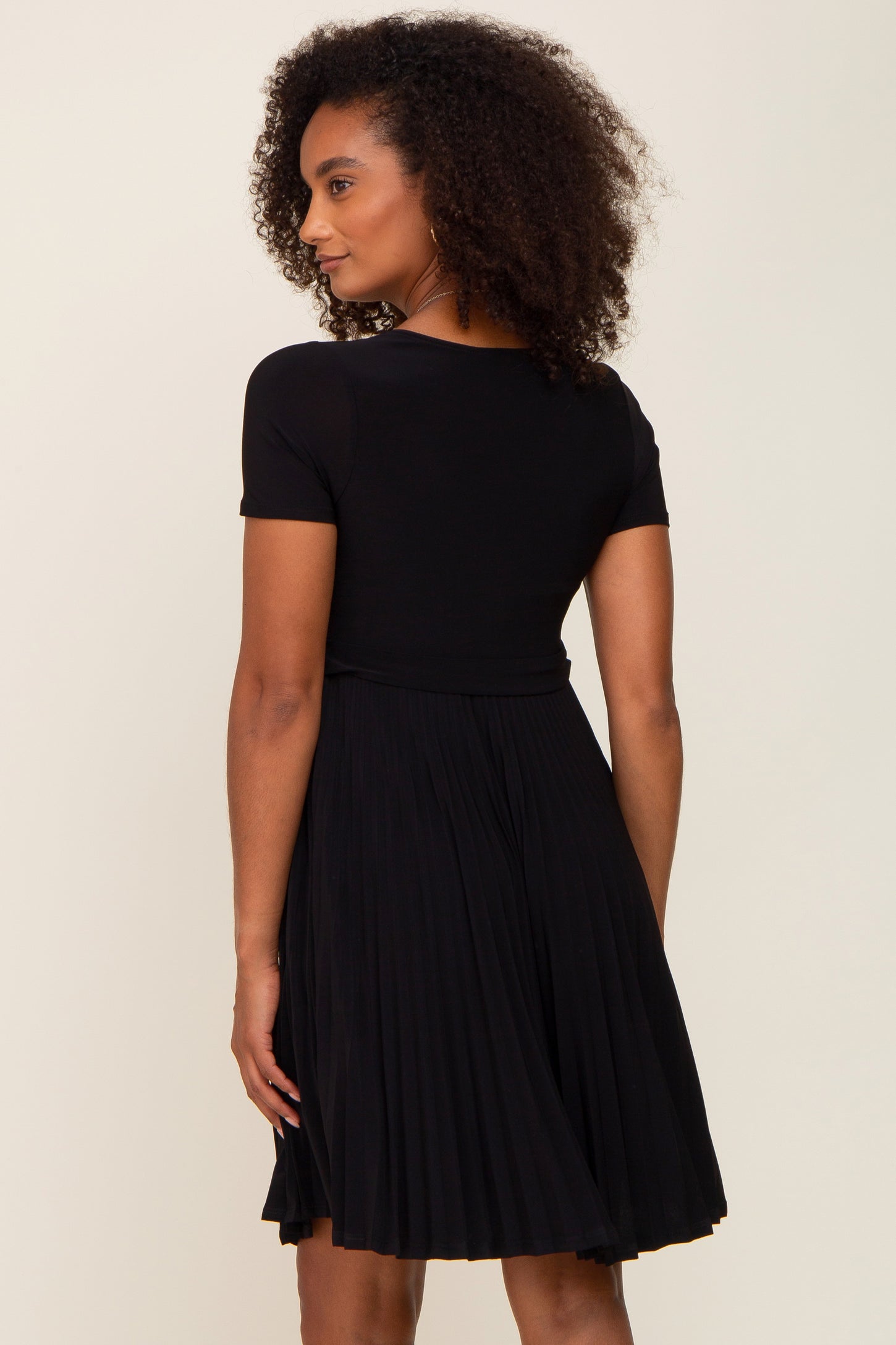 woman wearing a black short sleeve pleated dress, showing the back view and natural curly hair
