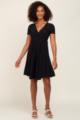 woman wearing a short sleeve black pleated maternity dress with a v-neckline and white block heel sandals