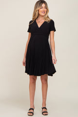 woman wearing a black short sleeve maternity dress with a pleated skirt and a fitted bodice, showing her baby bump
