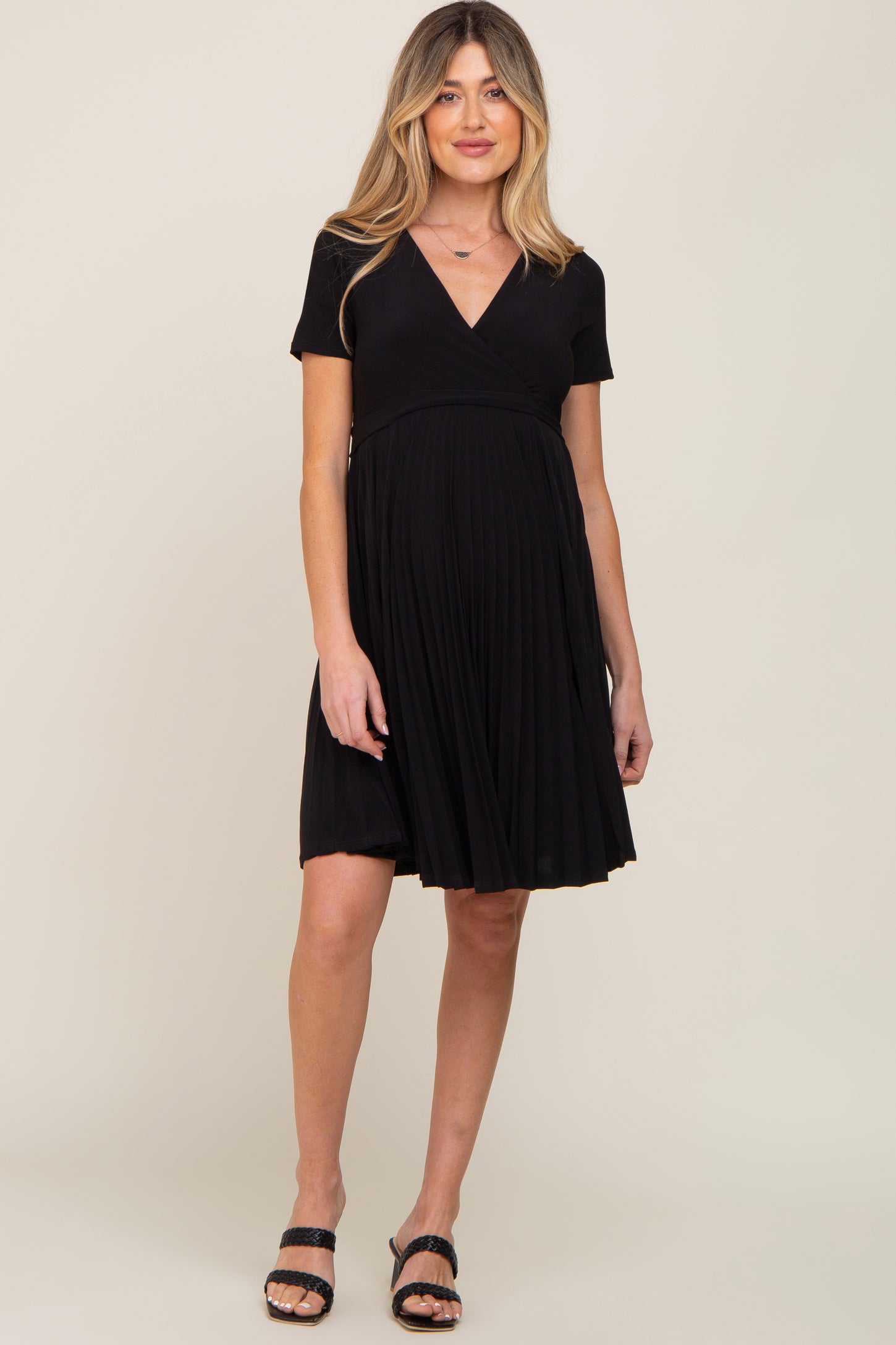 woman wearing a black short sleeve maternity dress with a pleated skirt and a visible baby bump