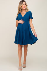 woman wearing a teal maternity dress with short sleeves and a pleated skirt, holding her baby bump