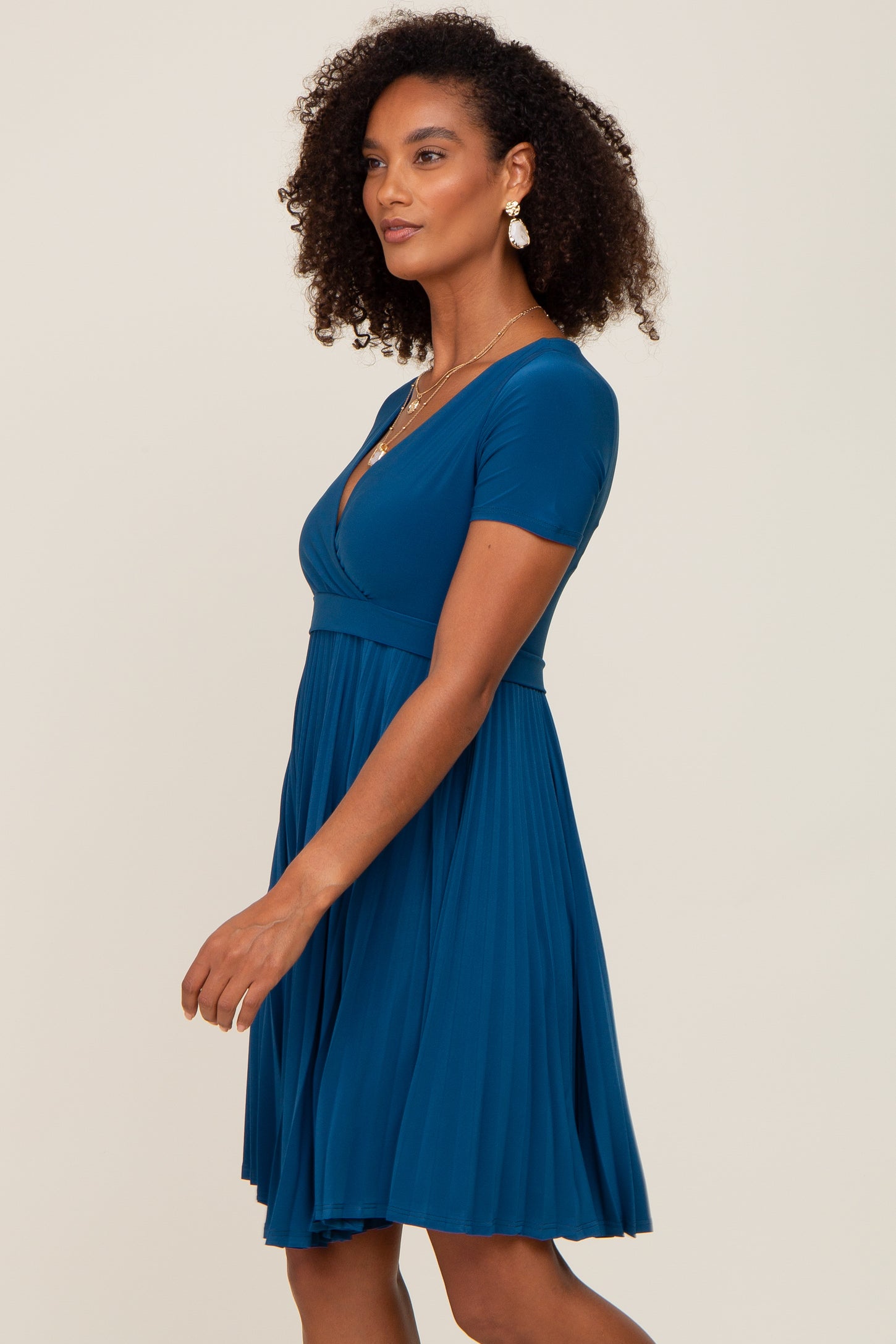 woman wearing a teal short sleeve dress with a fitted bodice and flared skirt, styled with curly hair and earrings