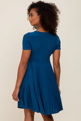 woman wearing a teal short sleeve pleated dress, shown from the back