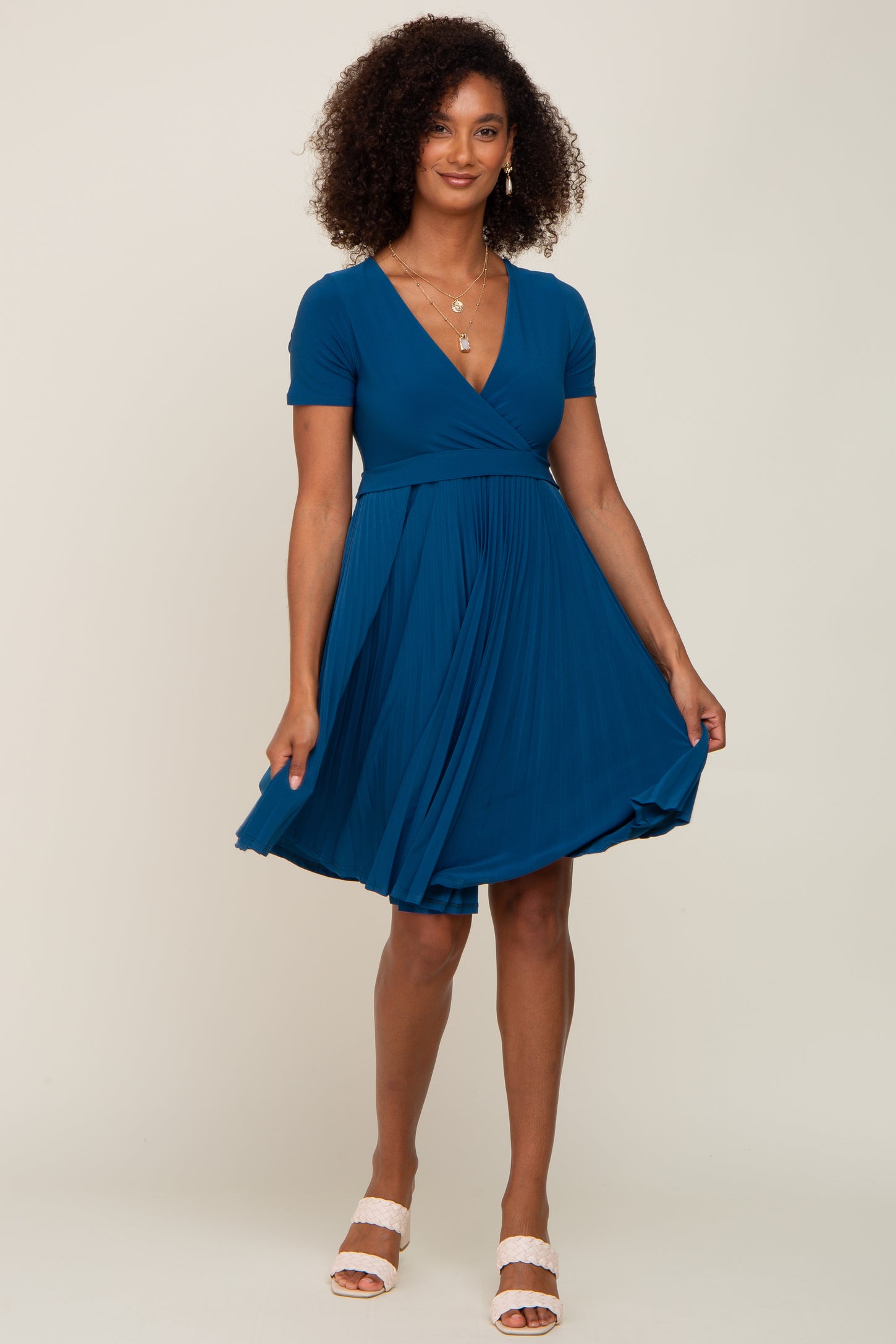 woman wearing a teal short sleeve wrap dress with a pleated skirt and a flattering silhouette