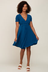 woman wearing a teal short sleeve wrap dress with a pleated skirt and a flattering silhouette