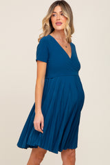 woman wearing a teal maternity dress with short sleeves and a pleated skirt, showcasing her baby bump