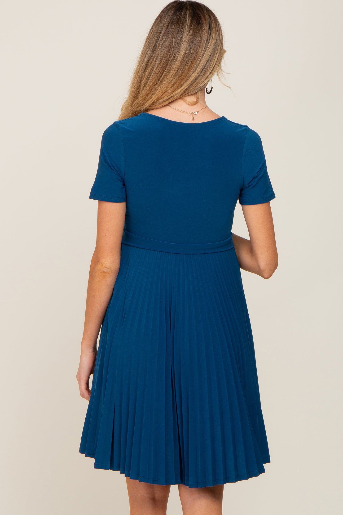 woman wearing a teal short sleeve maternity dress with a pleated skirt from the back