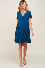 woman wearing a teal short sleeve maternity dress with a pleated skirt and a v-neckline, highlighting her baby bump