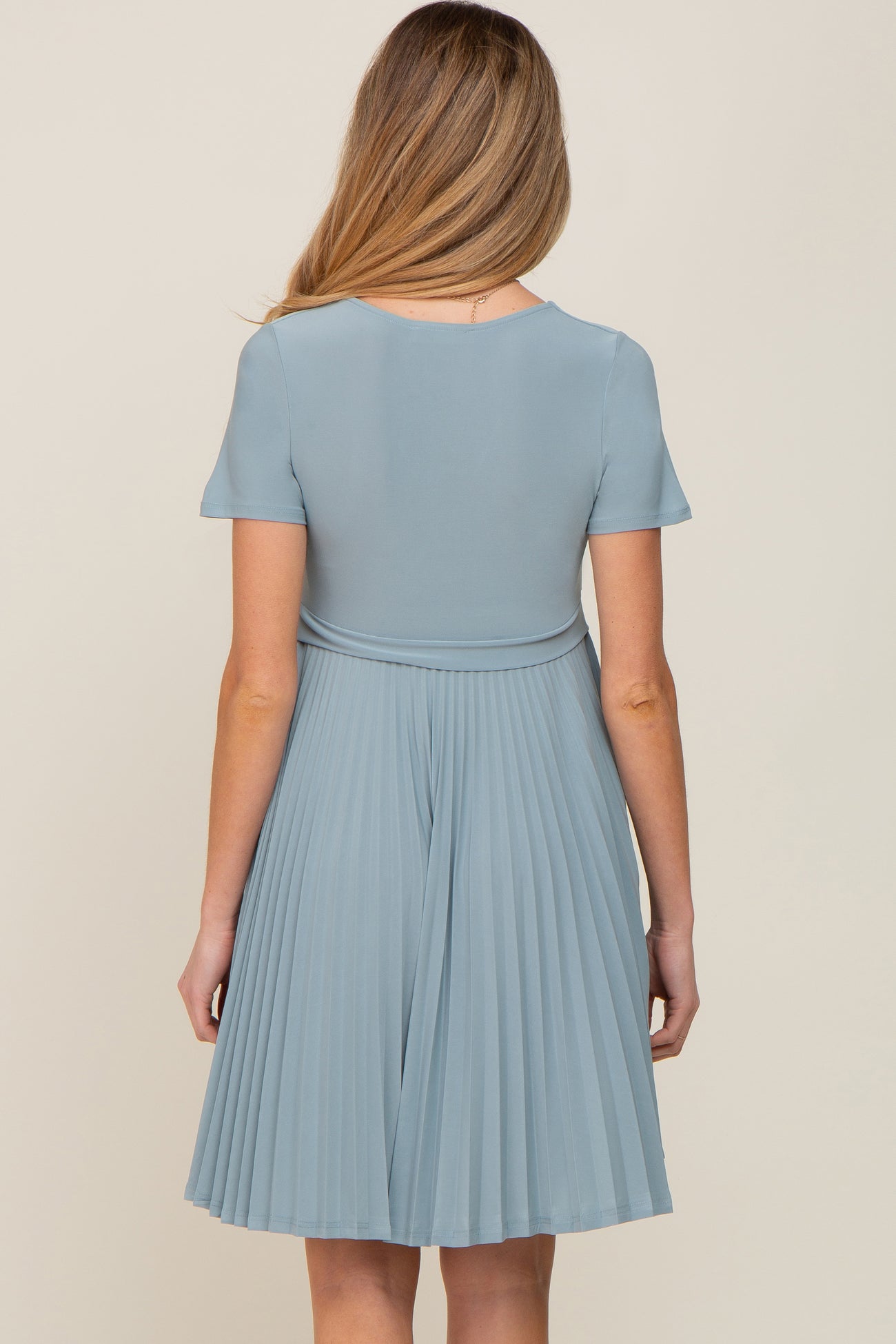 woman wearing a light blue pleated maternity dress with short sleeves, showing the back view