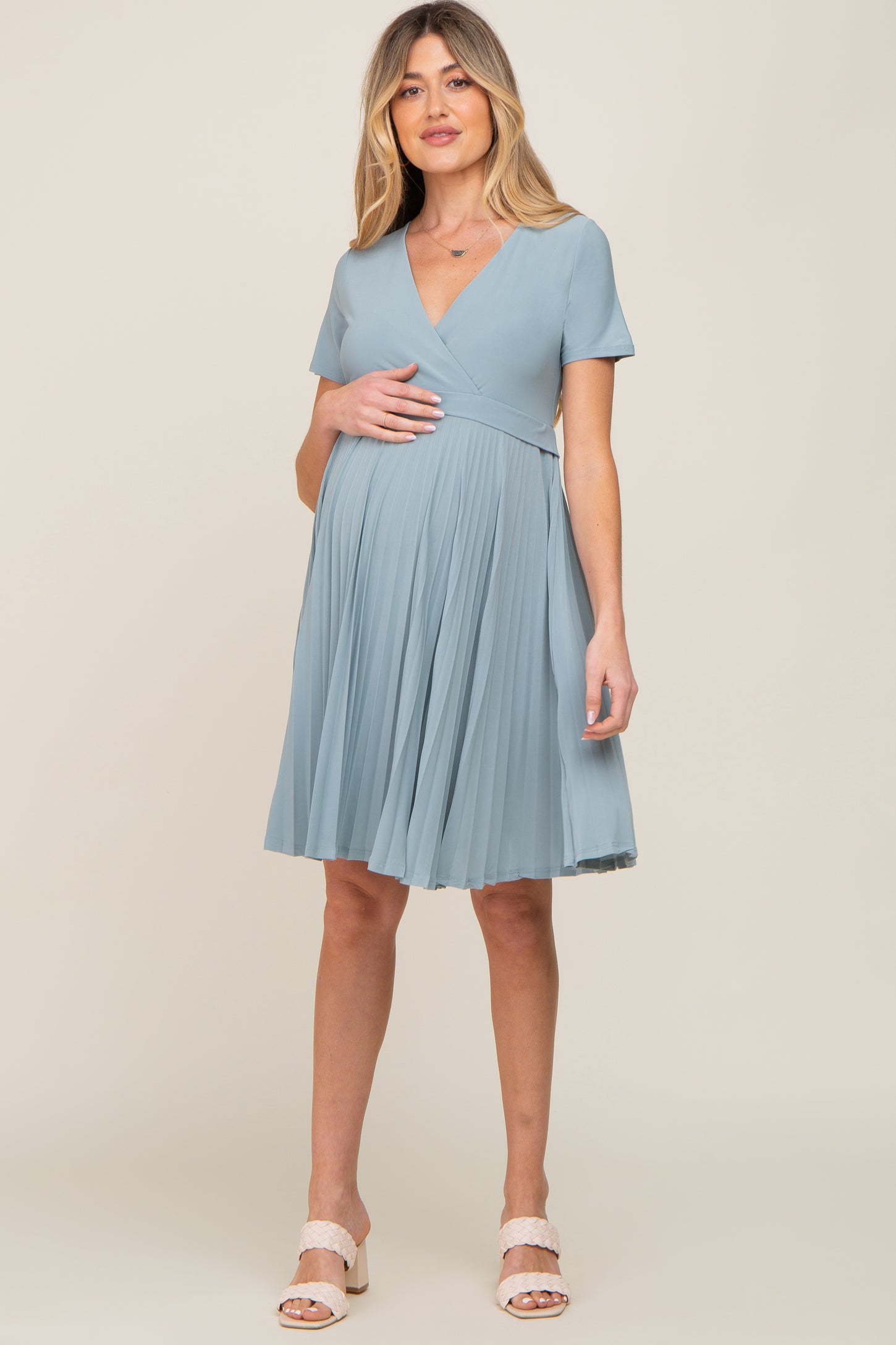woman wearing a light blue short sleeve maternity dress with a pleated skirt and visible baby bump