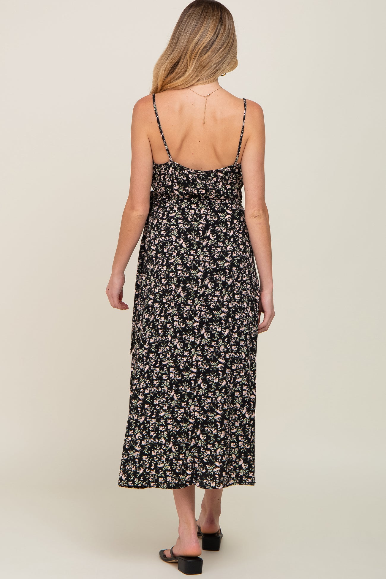 Back view of a woman wearing a black floral midi dress with spaghetti straps and sandals