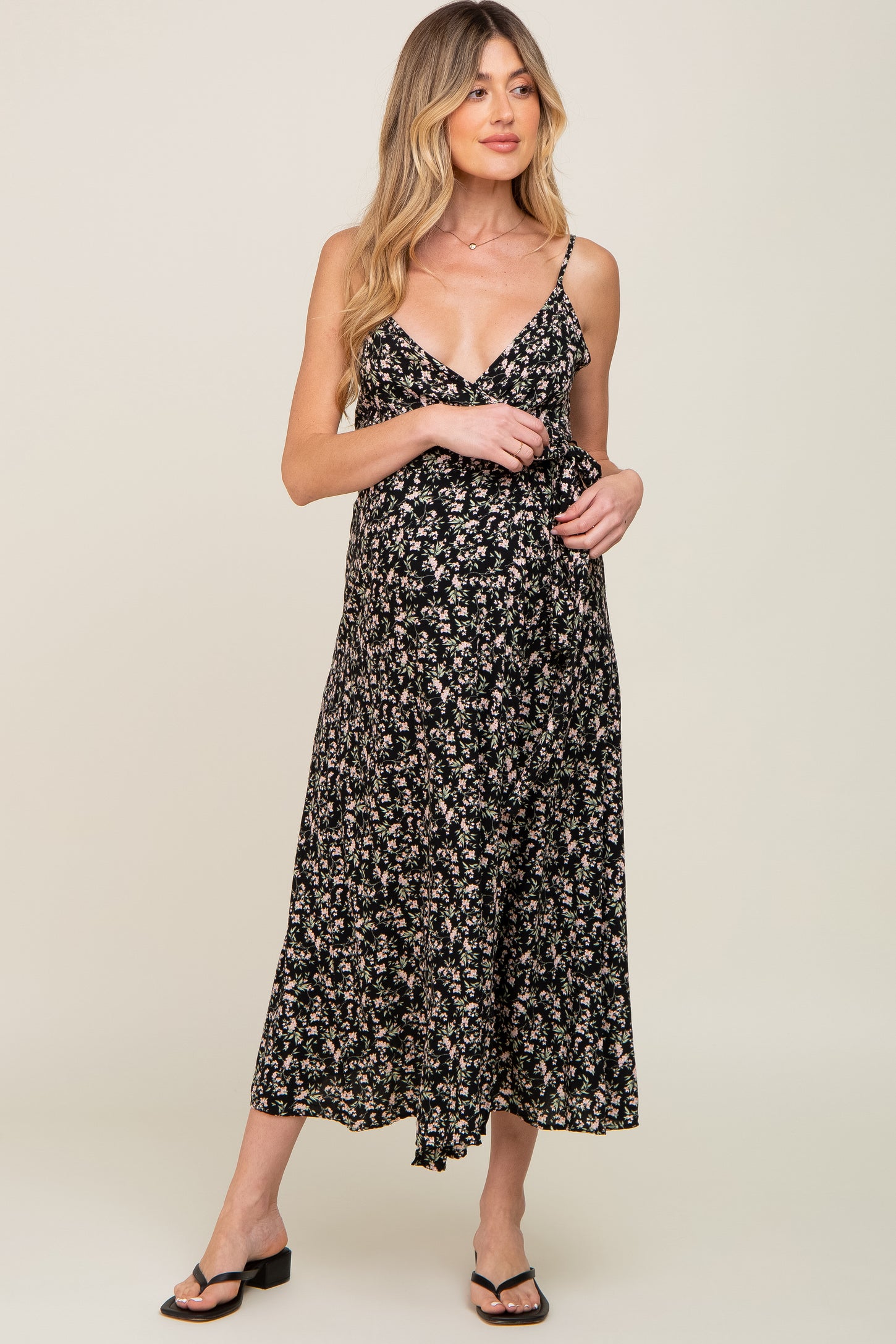 Woman wearing a black floral maternity midi dress with spaghetti straps and a wrap waist design