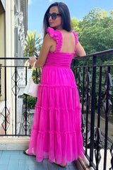 woman wearing a hot pink tiered maxi dress with ruffle straps, standing on a balcony with greenery in the background