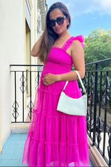 woman wearing a hot pink maternity maxi dress with ruffles and sheer layers, holding a light green handbag and posing outdoors